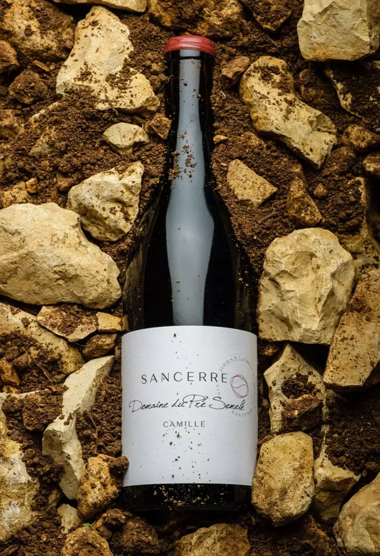 Bouteille de la cuvée Camille posée sur le terroir du Domaine du Pré Semelé