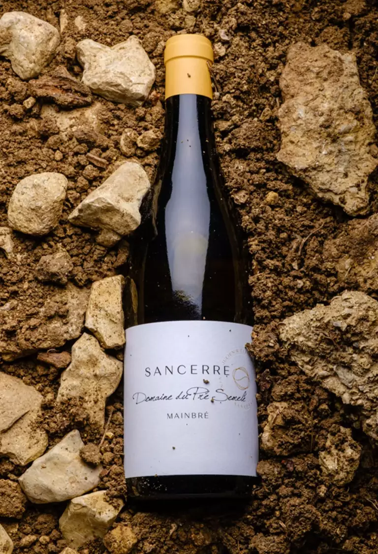 Bouteille de Mainbré Blanc posée sur le terroir du Domaine du Pré Semelé